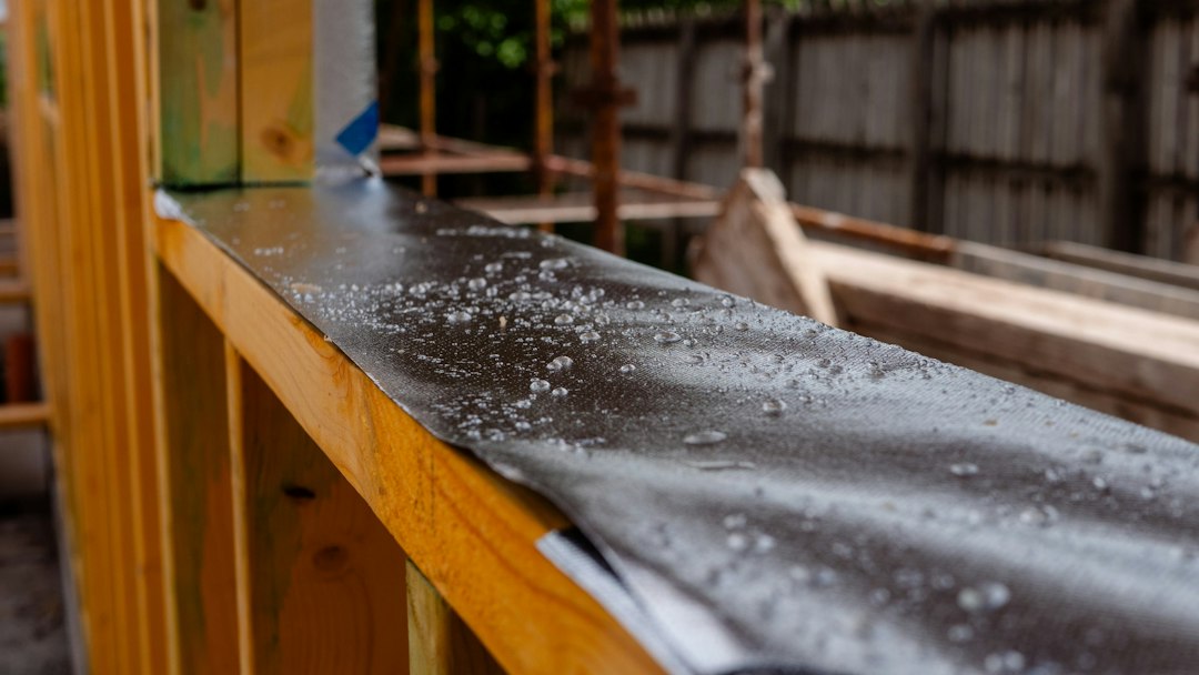 Raindrops on a black waterproof membrane covering a wooden wall frame