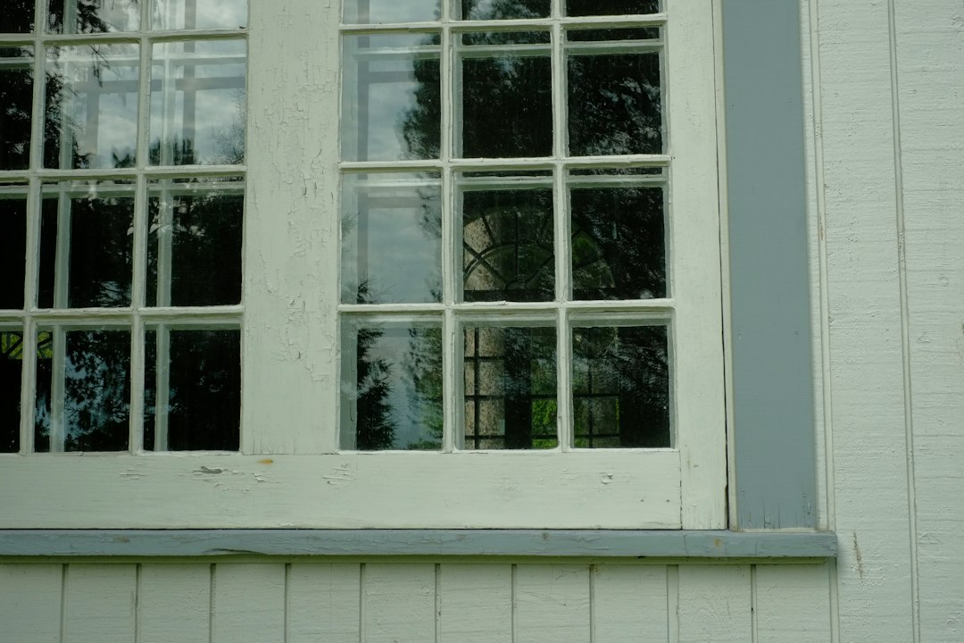 A white wooden window frame with peeling paint on a light green wall